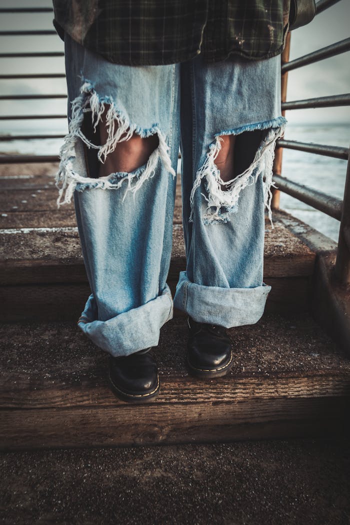 services-03 Close-up of ripped jeans and black boots on wooden stairs with metal railings.