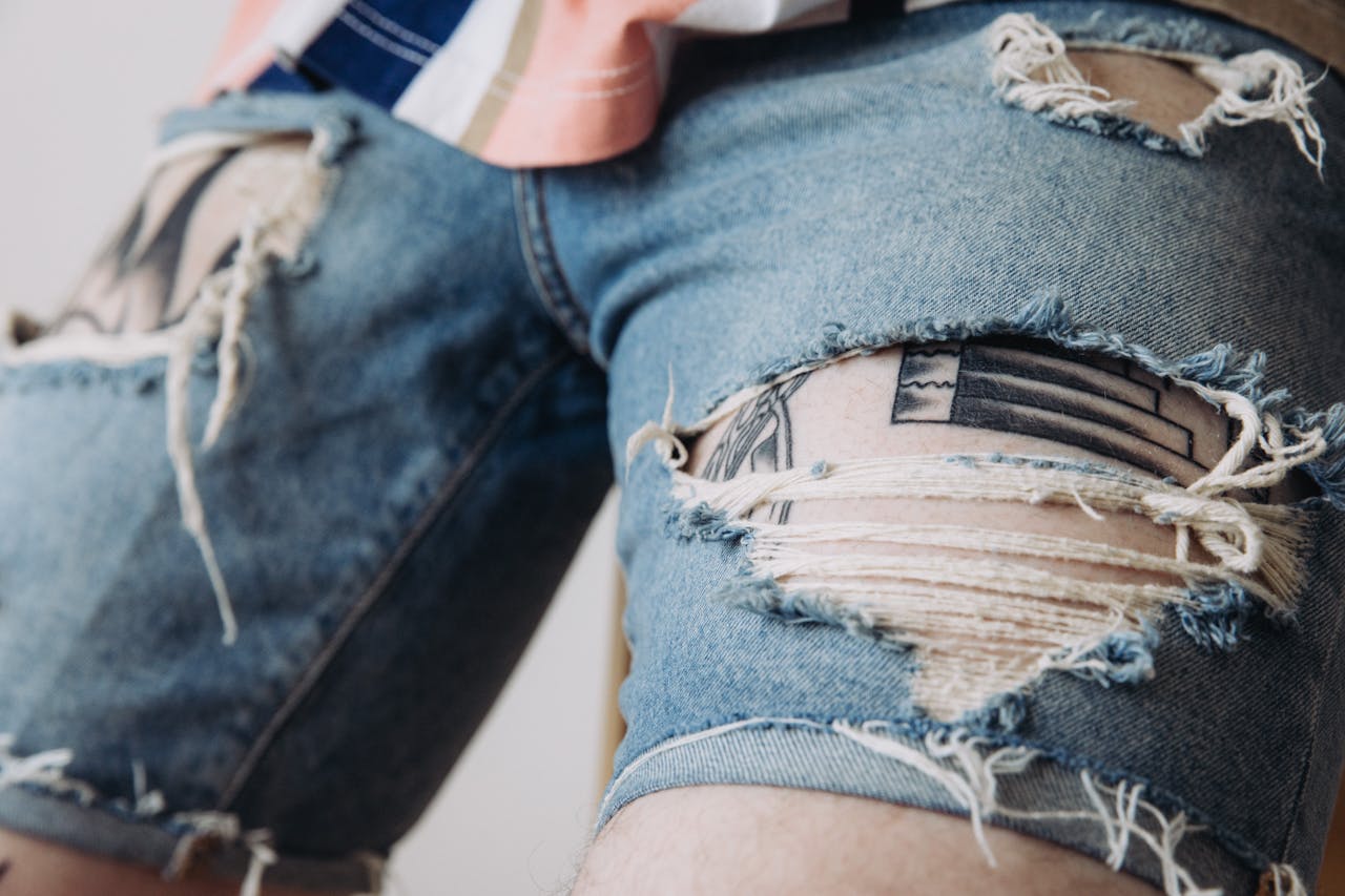hero-img-02 Detailed view of worn denim shorts with tattoos peeking through, showcasing unique style.
